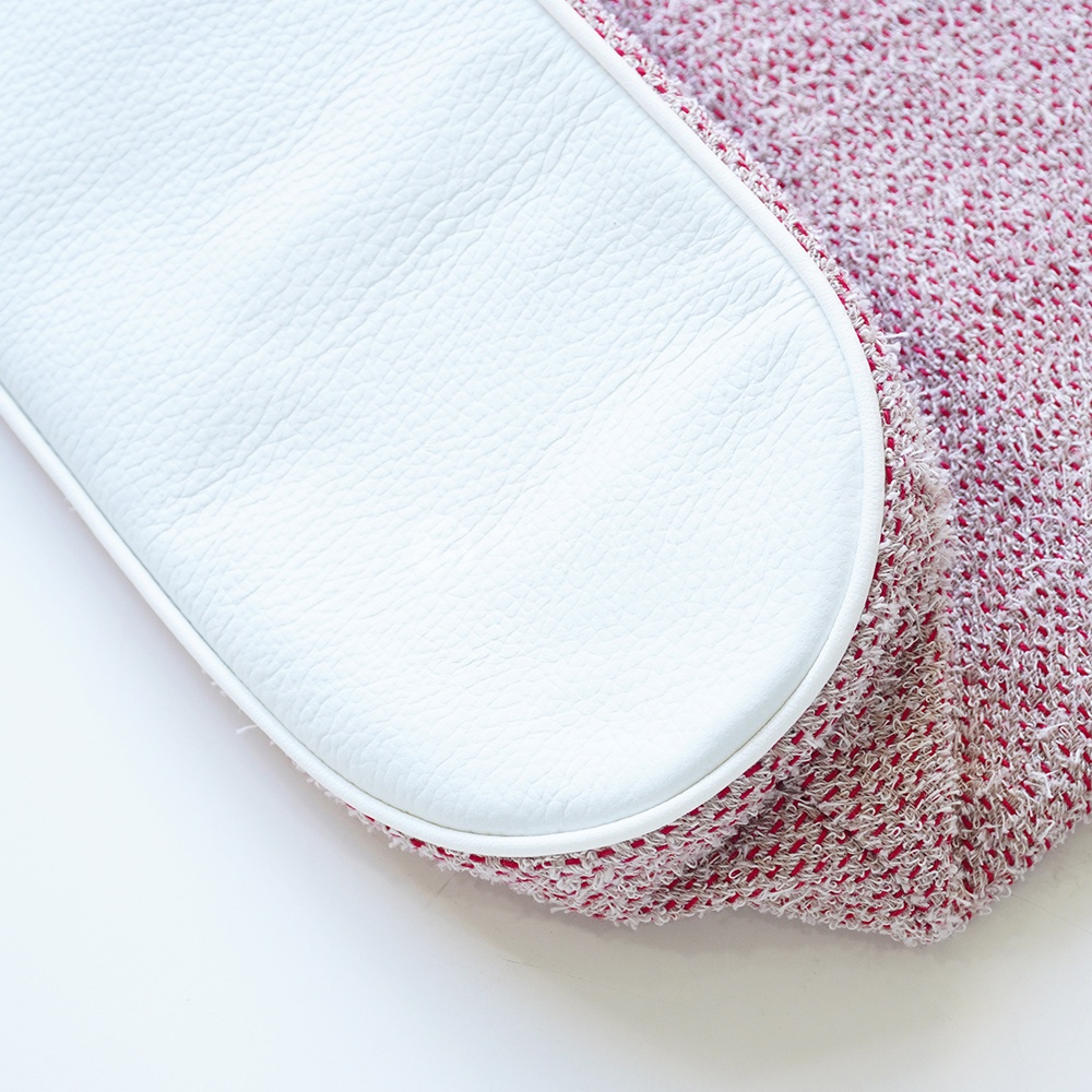 特寫鏡頭展示一個有紋理的白色皮革墊，鋪設在紅色和白色混紡的網狀織物上，織物邊緣有磨損。