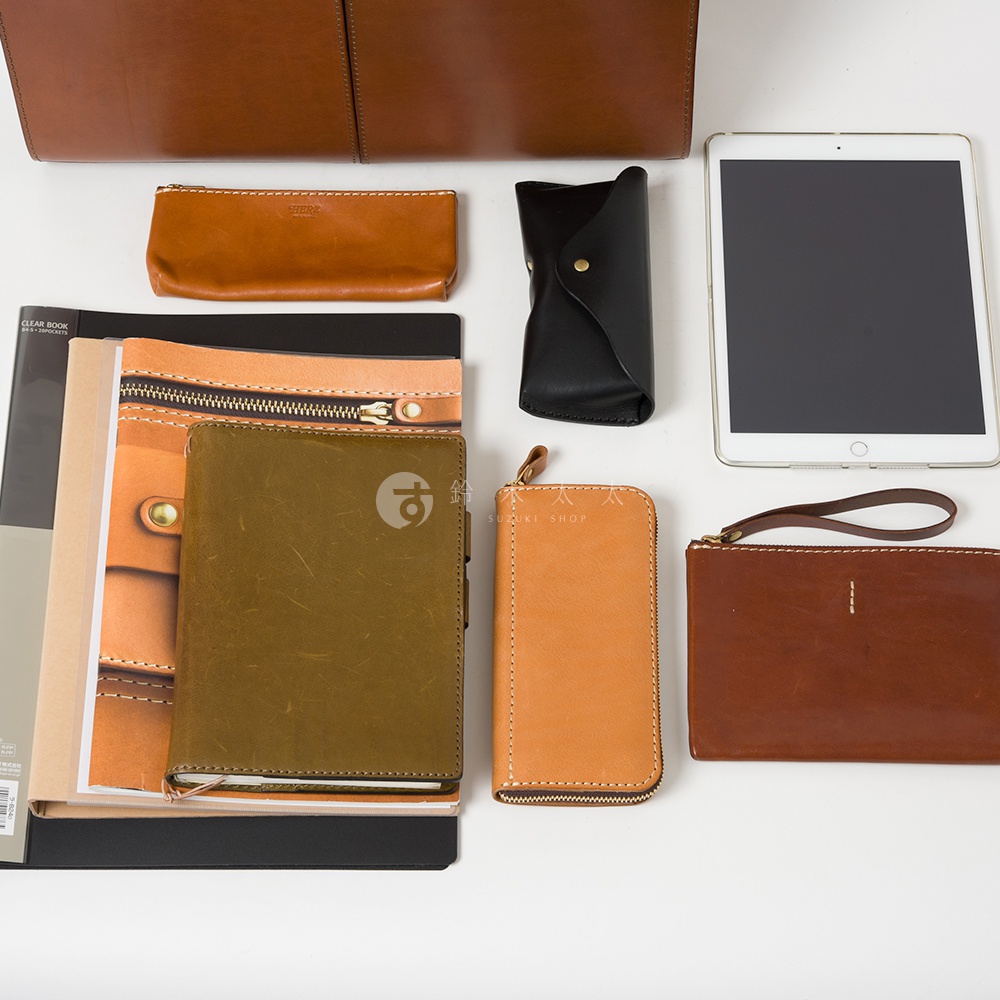 職人手作皮革雙口袋兩用商務公事包 BW-20，展示出不同尺寸與顏色的配件，包含棕色、橘色、綠色及黑色的皮革小物，如筆袋、筆記本、平板電腦保護套及長夾。