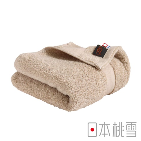 米色今治匹馬棉毛巾，柔軟蓬鬆，質感細膩，帶有黑色品牌標籤，標籤上印有金色字體「HOTEL Grand」，上方有紅藍色細線裝飾。