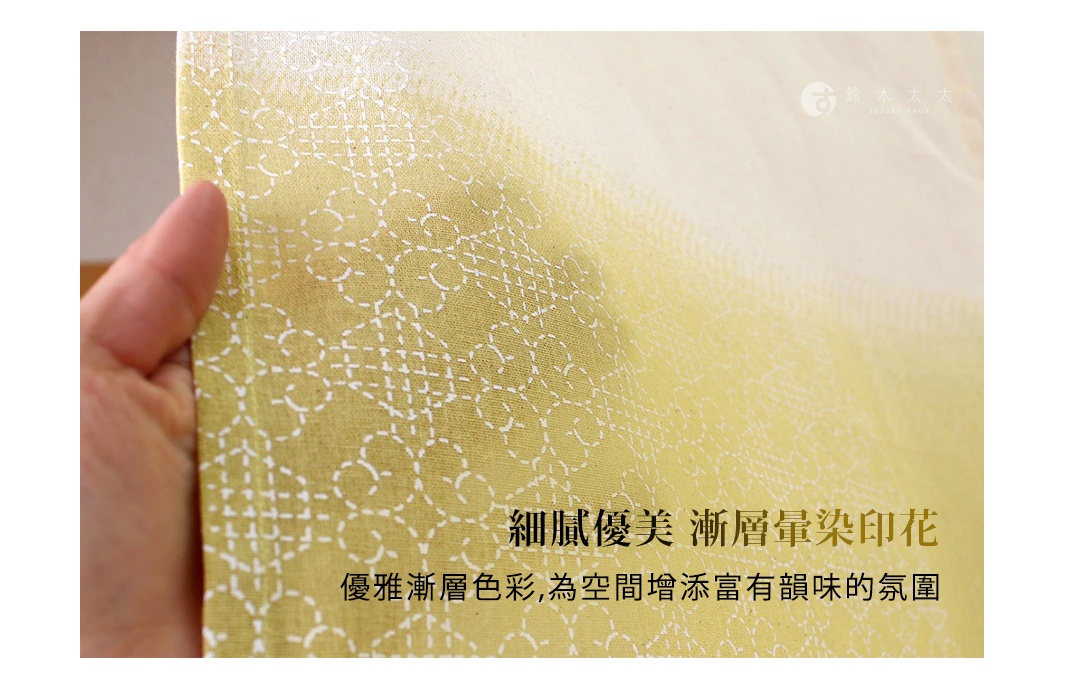 一隻手正輕輕拉開一塊具有日式刺子繡花紋的門簾，布料呈現出柔和的黃色漸層暈染效果，透過細膩的印花設計與透光質感，為空間營造出充滿日系禪意的溫馨氛圍。