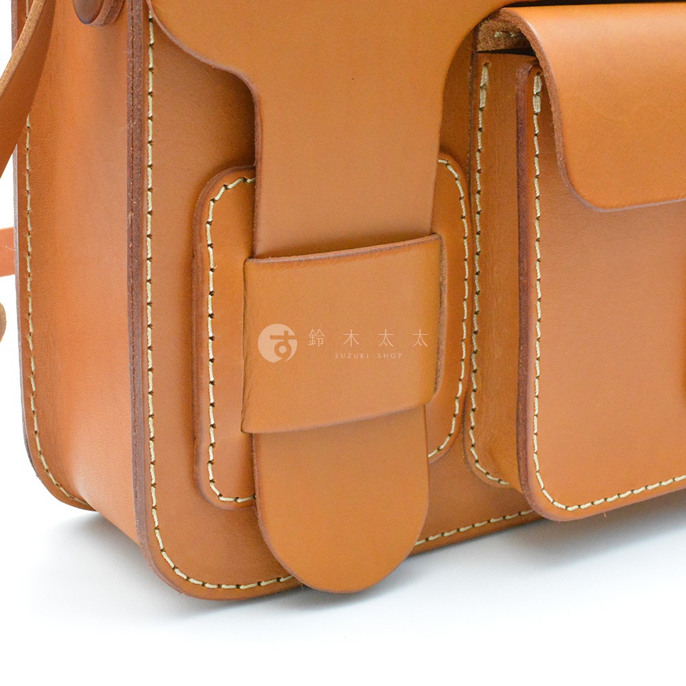 棕色皮革單肩包，有明顯的縫線細節，正面有兩個翻蓋式口袋，其中一個口袋上方有一個額外的皮革搭扣。