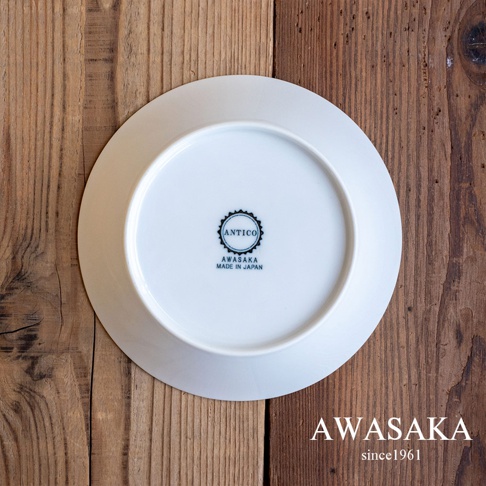 白色圓形陶瓷盤，底部印有黑色「ANTICO AWASAKA MADE IN JAPAN」字樣，盤子置於木紋背景上。