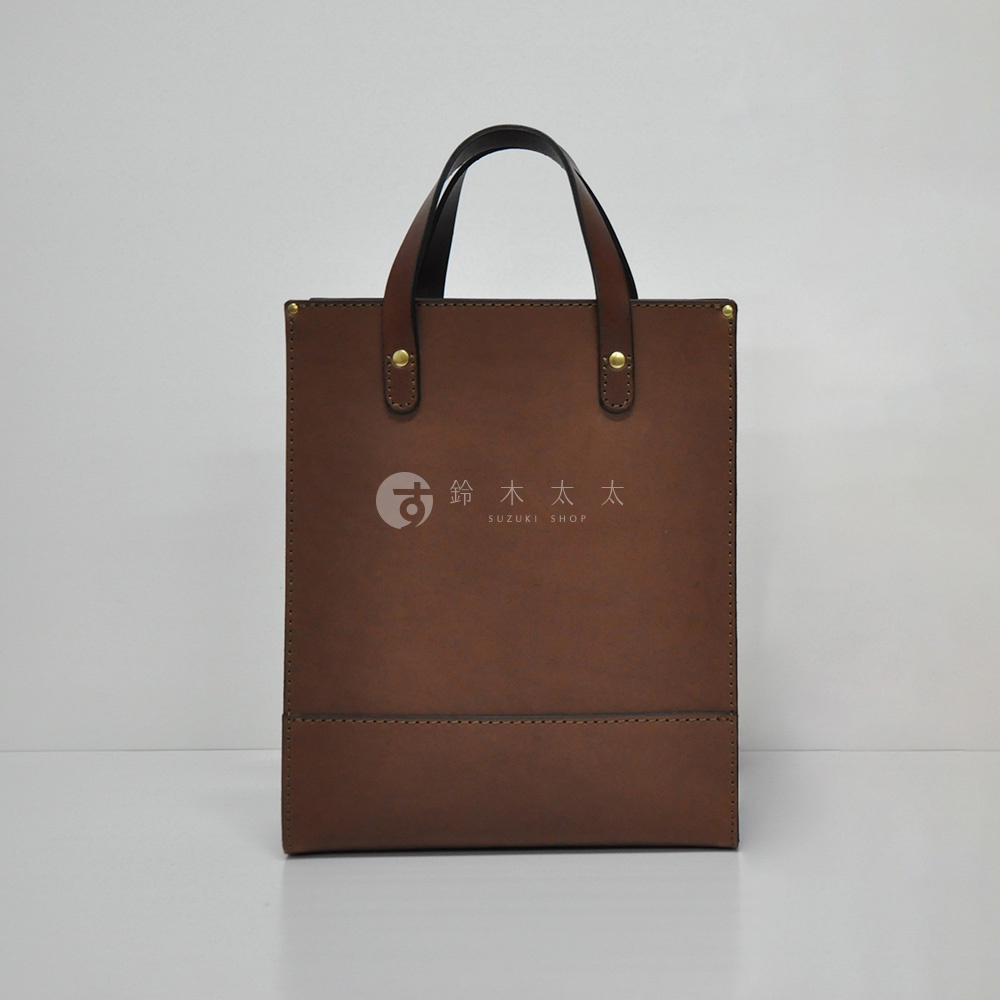 職人手作皮革直式托特包，採用咖啡色皮革製作，包身直立，配有雙提把，包面中央有品牌Logo壓印。