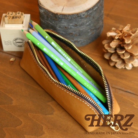 職人手作皮革三角收納筆袋，淺棕色皮革，內含多色鉛筆，金屬拉鍊，簡約設計。