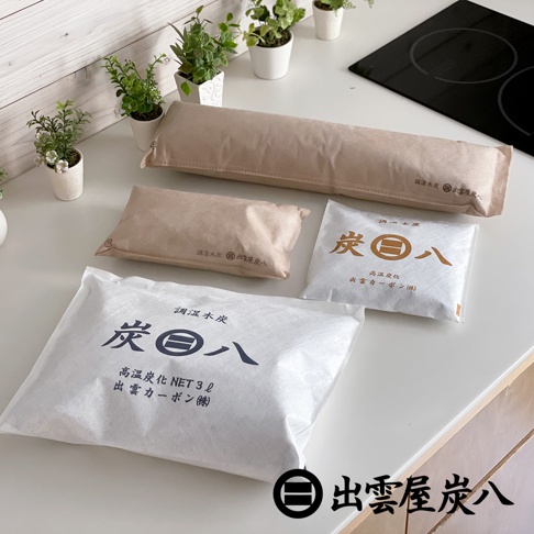 多個尺寸的車內調濕木炭包，以米色和白色無紡布製成，上面印有黑色日文文字和標誌，周圍散佈著綠色植物和白色盆栽。