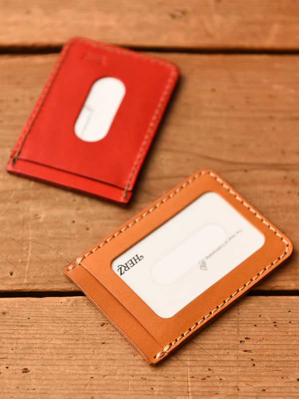 兩個職人手作皮革直式票券收納夾，一個為亮紅色，另一個為棕褐色。兩者均為皮革材質，邊緣車縫線清晰，並有透明視窗可放入卡片或票券。