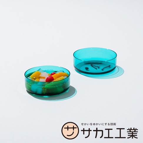 SAKAE 兩款藍綠色玻璃碗，其中一個盛有什錦水果果凍，另一個碗內有黑色細長物體，下方有日文品牌標識「サカエ工業」。