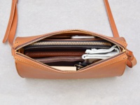 棕色皮革拉鍊單肩包，打開的內層展示了手機、錢包、卡夾和零散小物，搭配金屬拉鍊和細緻縫線。