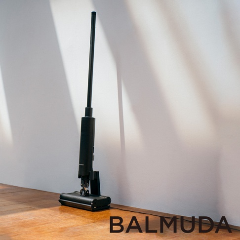 The Cleaner 無線吸塵器 (黑色) 是一款黑色、簡約設計的無線直立式吸塵器，配有細長的黑色吸塵桿和底部黑色方形吸頭，立於木質地板上，背景為白色牆壁。