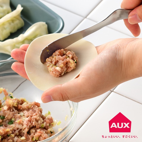 手持不鏽鋼果醬抹刀，將肉餡填入水餃皮中。背景有水餃和裝有肉餡的玻璃碗。