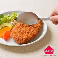 銀色金屬材質的leye 切切分食匙，正用來夾取盤中一塊金黃酥脆的炸物排。盤中另有生菜沙拉、烤地瓜片和紅蘿蔔塊。