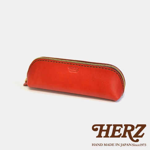 紅色職人手作皮革三角收納筆袋，採用拉鍊開合，表面壓有品牌標誌。