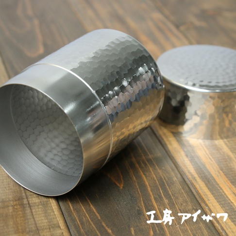 不鏽鋼錘目紋茶葉罐，銀色，表面有蜂窩狀錘擊紋理，罐身兩側有光滑的銀色飾帶。