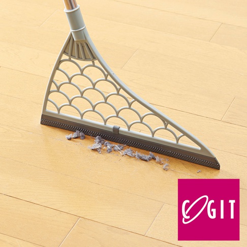 淺灰色三角形掃帚，帶有魚鱗狀鏤空設計，底部為深灰色橡膠刮條，正在清掃木地板上的灰塵。