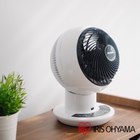 白色圓球形空氣循環扇，黑色扇網，帶有 IRIS OHYAMA 標誌，放置在木質桌面，背景為白色牆壁，左側有一盆綠色植物。