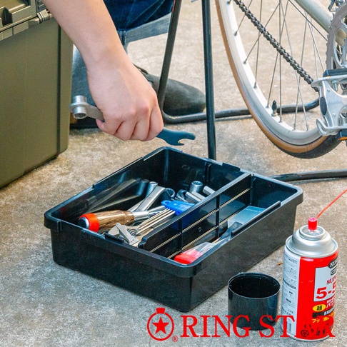 黑色塑膠工具箱內有各式扳手、螺絲起子和藍色零件，箱子旁有一罐紅色噴霧罐和一個黑色杯子。
