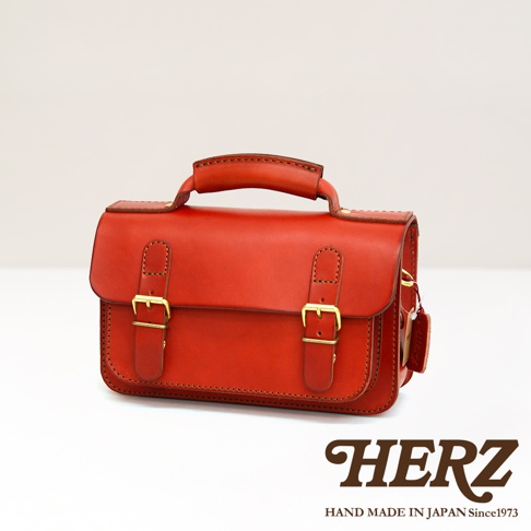 職人手作皮革雙扣兩用迷你肩背包，採用紅色皮革，設有金色搭扣和頂部提把，風格簡潔。