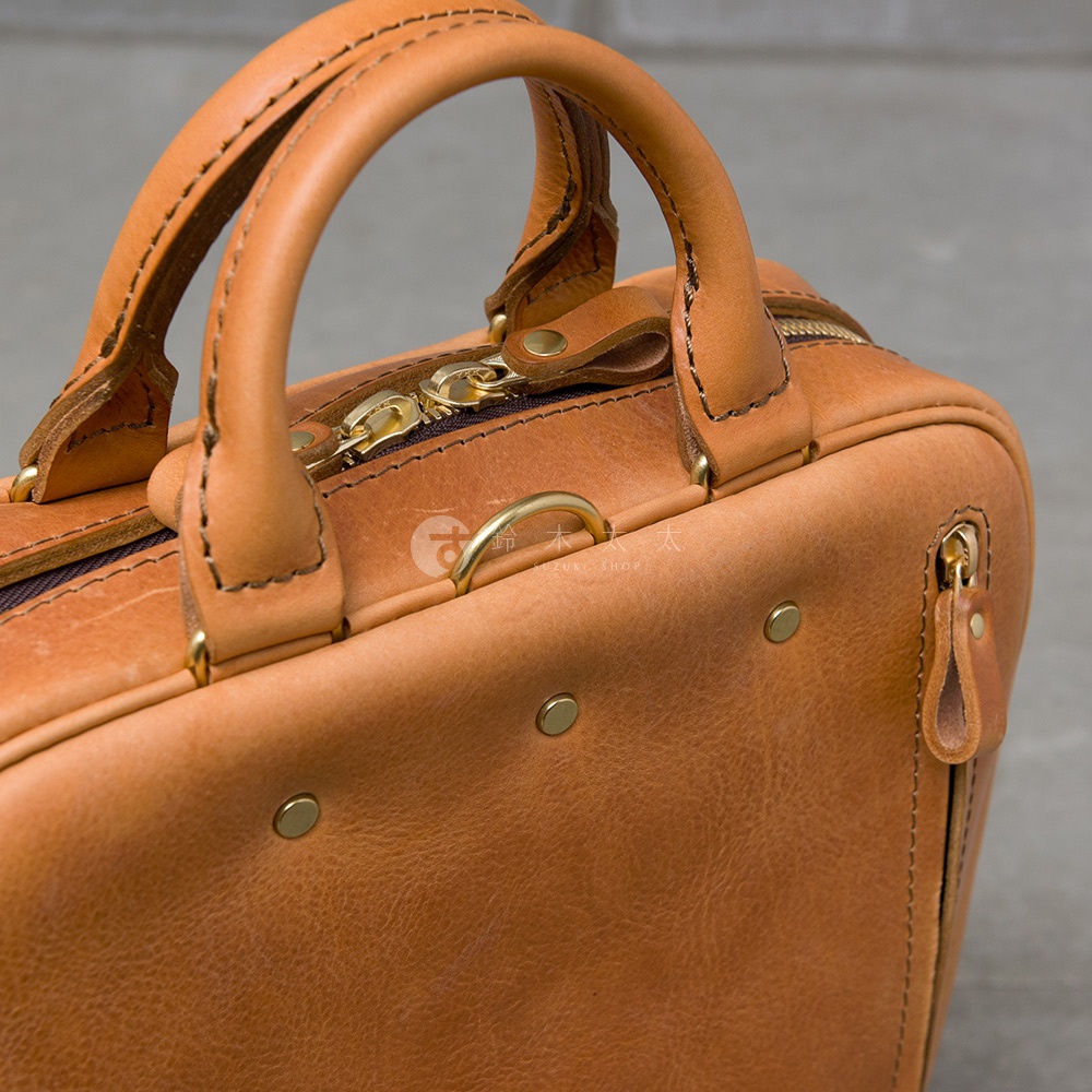 職人手作皮革Organ商務後背包，特寫其溫潤的焦糖色皮革、精緻的車縫線、黃銅色拉鍊與五金配件，以及提把與包身連結處的細節。