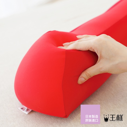 一個紅色的舒背拉伸枕，材質柔軟，有一個凹陷處，被一隻手輕輕按壓。