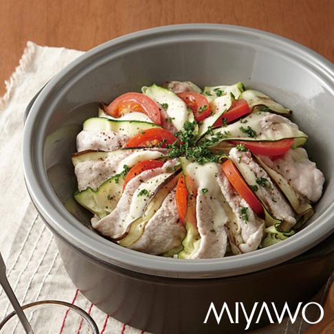 深灰色陶土鍋內盛裝著一道由雞肉片、櫛瓜片和番茄片堆疊而成的料理，表面撒有香草碎。