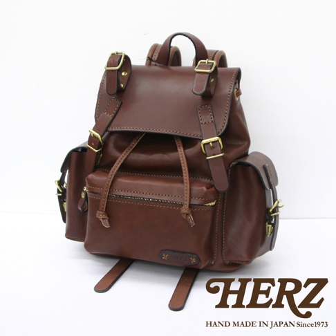 職人手作棕色皮革復古旅行後背包，帶有金屬扣環和抽繩閉合，側面有兩個小口袋，整體呈現經典復古風格。