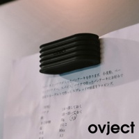 黑色矽膠鍋蓋，側面有條紋設計，印有「OVJECT」品牌字樣，放置於印有日文食譜的紙張上。