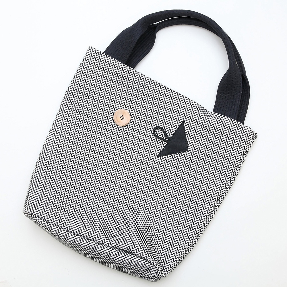 直式收納托特包，黑白細小格紋刺子織布面，配有黑色提把，包身有一個木質鈕扣及一個黑色三角形裝飾。