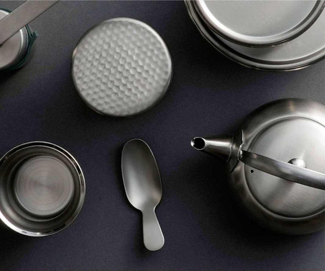 日製18-8不鏽鋼茶葉罐，罐蓋有錘目紋，附帶一個同材質的茶匙，整體呈銀灰色。