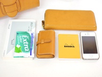 數件原色皮革小物，包含長夾、鑰匙包、手機、筆記本及口香糖，皆以白色背景呈現。