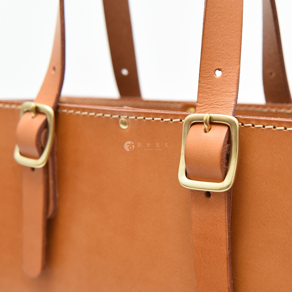咖啡色皮革托特包，配有可調節的皮革提把和黃銅色釦環，展現職人手作的精緻工藝。