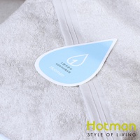 淺灰色毛巾，材質為柔軟棉質，表面有細緻的絨毛。一張藍色水滴狀吊牌，上面印有日文「1秒タオル 大切なのは吸水性」及英文「Hotman」品牌名稱。