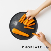 黑色圓形CHOPLATE兩用砧板盤上，擺放著一整根胡蘿蔔和多段切好的胡蘿蔔。兩隻手正在拿取胡蘿蔔。