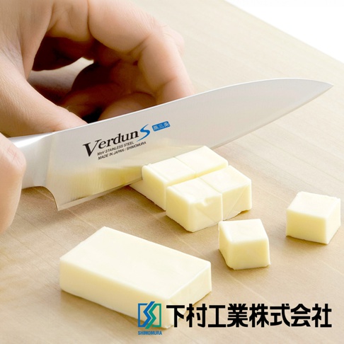 VERDUN S 不鏽鋼水果刀，刀身有「Verdun S」和「MoV STAINLESS STEEL MADE IN JAPAN / SHIMOMURA」字樣，正在切分塊狀的黃油，刀刃鋒利，背景為木質砧板，右下角有「下村工業株式會社」的標誌。