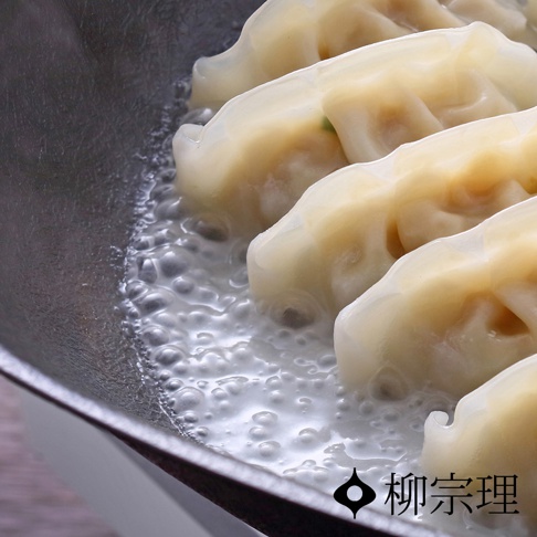 鐵鍋中排列整齊的煎餃正在烹飪，鍋底水分沸騰形成氣泡，右下角標示柳宗理品牌標誌，整體呈現煎煮食物的特寫視角。