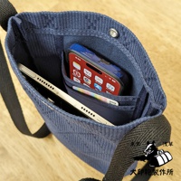 深藍色刺子織紋理的平板收納側背包，主隔層內有手機與平板電腦，背包外側有兩個收納袋，肩帶為黑色寬織帶。