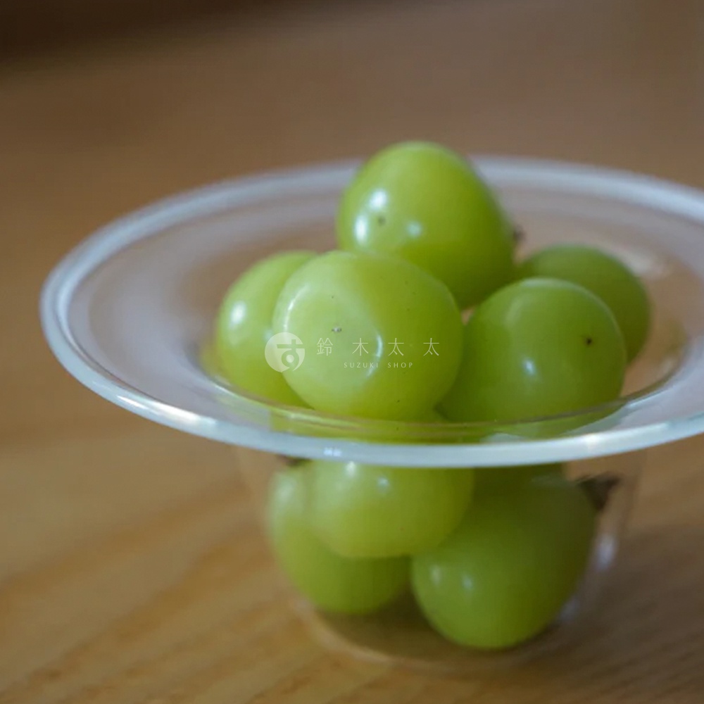 一個透明玻璃製成的深型點心碗，盛裝著數顆綠色葡萄，碗緣有細微的弧度。