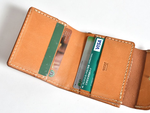 淺棕色皮革方形短夾，內有卡槽，可見兩張信用卡，其中一張為VISA卡，另一張為星巴克卡。皮革表面有自然紋理，縫線工整。