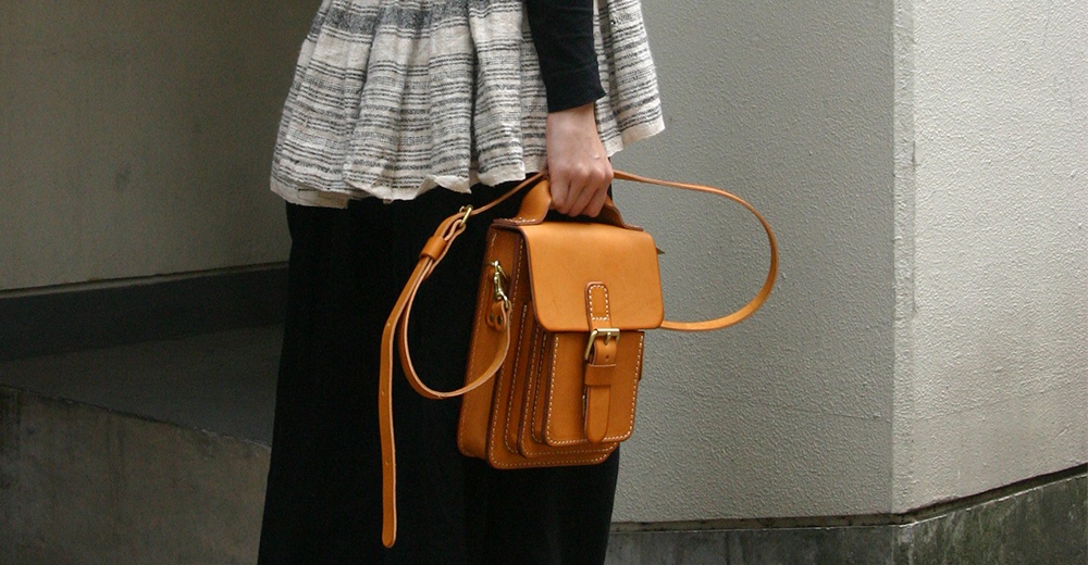 一只棕褐色皮革製成的手提包，帶有可拆卸的長肩帶，包身有縫線細節和金屬釦。