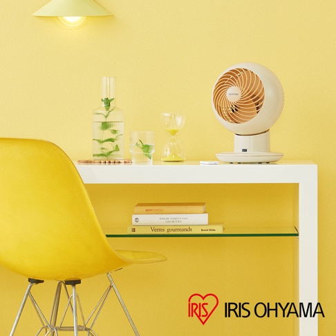 米色圓形空氣循環扇，帶有風扇葉片，放置在白色層架上，旁邊是玻璃瓶、玻璃杯和沙漏。