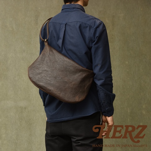 職人手作皮革Organ單肩半月包，深棕色，採用紋理皮革製成，斜背於身穿深藍色襯衫的男子身上。