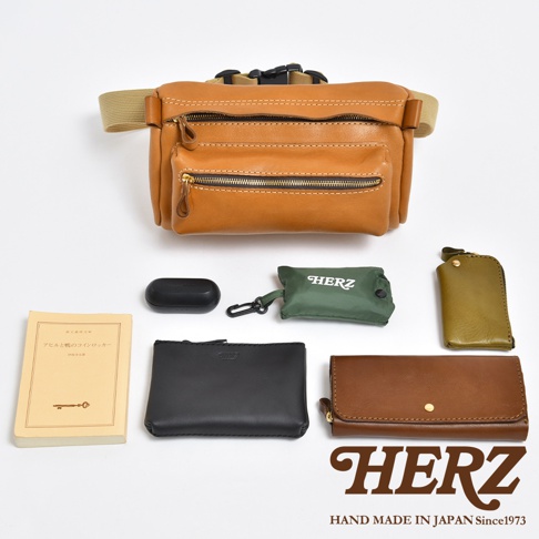 職人手作皮革兩用腰掛斜背包，展示了棕褐色皮革材質、雙拉鍊前袋、可調節腰帶，以及搭配的黑色無線耳機盒、綠色收納袋、橄欖綠鑰匙包、黑色皮夾和棕色長夾。