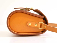 職人手作皮革皮扣單肩包，採用天然棕褐色皮革製成，質感細膩。包體呈現圓潤飽滿的曲線，搭配復古黃銅色皮扣及鉚釘，風格簡約大方。