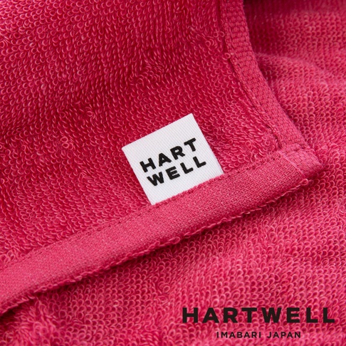 近拍的粉紅色毛巾，織紋清晰可見，上面縫有一個白色標籤，印有黑色字樣 HART WELL。
