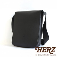 一個黑色皮革軟皮直式斜背包，上面印有「Z」字樣，底部有「HERZ HAND MADE IN JAPAN Since1973」的品牌標誌
