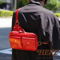 鮮紅色皮革雙口袋斜背包，附有拉鍊主袋，正面兩個翻蓋口袋，金屬扣環，肩帶可調節。