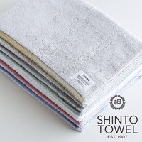 YUKINE 雪中漫步系列有機棉蓬厚迷你浴巾，堆疊展示，包含淺灰、米金、淺綠、淡粉、淺藍等多種顏色，質地蓬鬆柔軟，帶有品牌標籤。