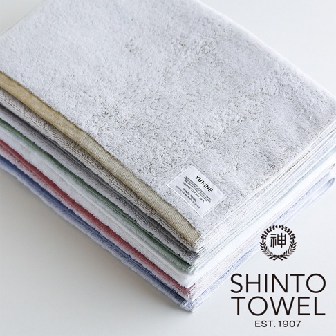 YUKINE 雪中漫步系列有機棉蓬厚迷你浴巾，堆疊展示，包含淺灰、米金、淺綠、淡粉、淺藍等多種顏色，質地蓬鬆柔軟，帶有品牌標籤。