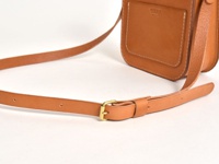 職人手作皮革翻蓋迷你單肩包，採用天然棕色皮革製成，配有可調節的皮質背帶，帶有黃銅色金屬扣環。包身有車縫線裝飾，翻蓋上壓印有品牌Logo。
