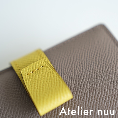 Atelier nuu 品牌字樣出現在灰色紋理皮革表面，黃色皮革翻蓋上有縫線細節