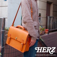 職人手作皮革經典三扣兩用商務公事包，亮橘色皮革，配有頂部提把、可拆卸肩帶、雙皮帶釦和金色轉鎖，風格復古。